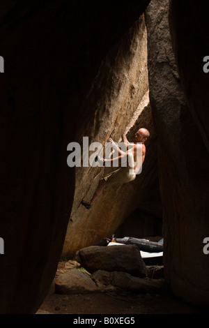 Männliche Felsen Kletterer Bouldern in Hampi Indien. Die Felsbrocken lehnen gegeneinander um eine Höhle zu bilden. Stockfoto