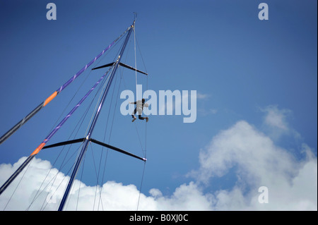 Ein Mann-Segler, Klettern auf den Mast einer Rennyacht, abgebildet in Plymouth, Devon. Stockfoto