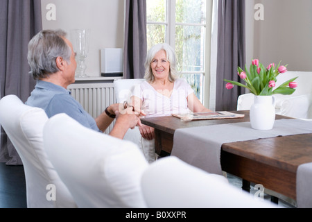 Senior paar sitzt am Tisch im Wohnzimmer, Lächeln, Porträt Stockfoto