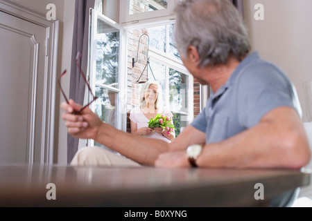 Senior Mann sitzt am Tisch, senior Frau stand in der Tür, Porträt Stockfoto