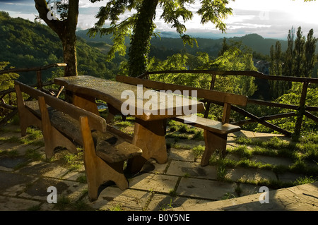 Holztisch und Bänken unter den Bäumen in einem Aussichtspunkt mit einem herrlichen Blick in einem grünen Tal in Italien Stockfoto