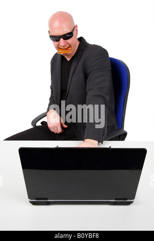 Glatze Mann mit Sonnenbrille und Kreditkarte in Mund sitzt vor einem Laptop geleitet Stockfoto
