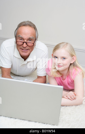 Großvater und Enkelin (8-9) auf Boden liegend, mit Laptop, Porträt Stockfoto