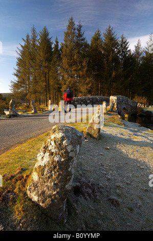 Eine Walker überquert den East Dart River über die alte Brücke der Steinstraße am Bellever auf einem kalten frostigen Winter Morgen Dartmoor UK Stockfoto