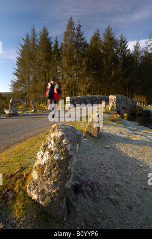 Ein Wanderer überquert den East Dart River auf der alten Steinstraße Brücke bei Bellever auf Dartmoor an einem kalten frostigen Morgen Devon UK Stockfoto