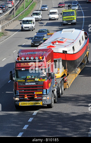 Scania LKW-Lkw fährt M25 m auf der Autobahn breite übergroße Bootsladung auf Tieflader, die auf die Autobahn-Zubringerstraße CONVOI AUSSERGEWÖHNLICHES Essex England UK trifft Stockfoto