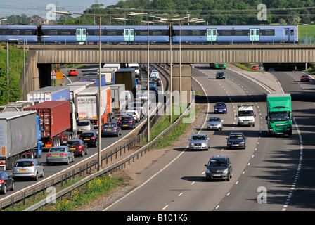 Transport Choice M25 Autobahn Nase zu Schwanz langsam Verkehr beobachten schnellen Personenzug auf Eisenbahnbrücke Kreuzung 28 Brentwood Essex England UK Stockfoto