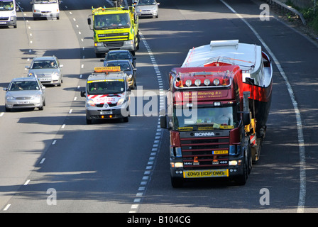 Scania LKW-Lkw fährt M25 m auf der Autobahn breite übergroße Bootsladung auf Tieflader, die auf die Autobahn-Zubringerstraße CONVOI AUSSERGEWÖHNLICHES Essex England UK trifft Stockfoto