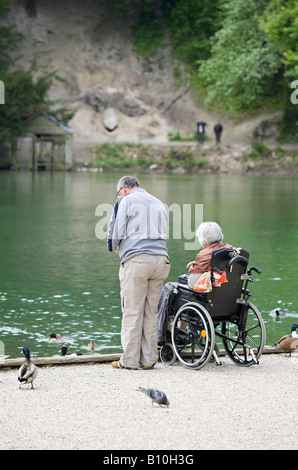 Ein älterer Mann mit Frau im Rollstuhl, der Enten am Swanbourne Lake, Arundel, West Sussex, England, Großbritannien füttert Stockfoto