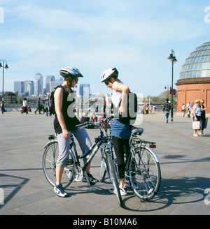 Radfahrerinnen befreundet sich mit jungen Frauen auf Fahrrädern in der Nähe des Eingangs zum Greenwich Foot Tunnel mit Canary Wharf in der Ferne London England Großbritannien KATHY DEWITT Stockfoto