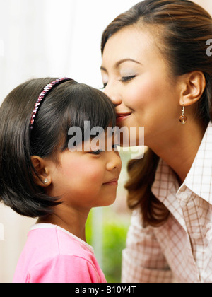 Eine junge asiatische Mutter küsst die Stirn der jungen Tochter Stockfoto