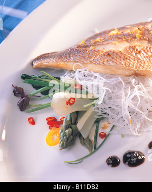 Asiatisches Meerbrasse Ofengericht, gebackene goldene Kruste mit verschiedenen Gratin-Saute-Gemüse-Auswahl an Chili-Gewürzen, serviert in einem weißen Teller mit blauem Handtuch Stockfoto