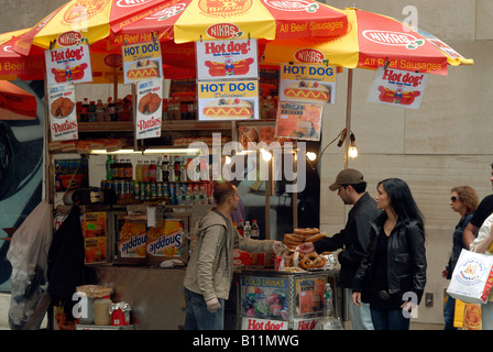 Touristen kaufen Würstchen und Brezeln aus einer New York Hot Dog Verkäufer auf der Fifth Avenue Stockfoto