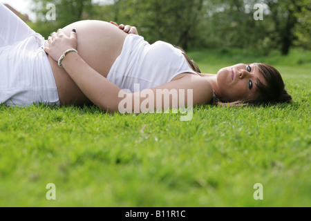 Glücklich schwanger 36 Woche Teenager-Mädchen alleine draußen auf dem Rasen liegen und hielt sie Magen ausgesetzt Stockfoto