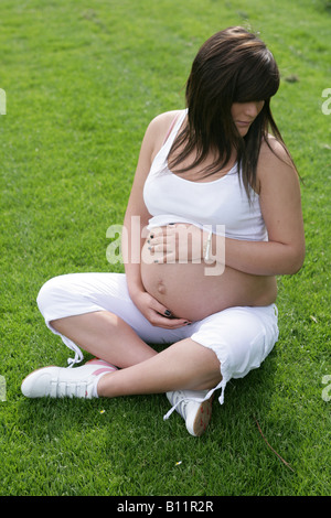 36 Woche schwangere Teenager-Mädchen alleine draußen sitzen und halten den exponierten Bauch Stockfoto