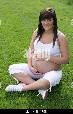 36 Woche schwangere Teenager-Mädchen alleine draußen sitzen und halten den exponierten Bauch Stockfoto