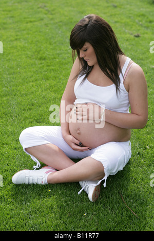 36 Woche schwangere Teenager-Mädchen alleine draußen sitzen und halten den exponierten Bauch Stockfoto