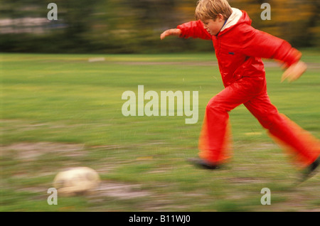 Ein neun Jahre alter Junge spielt Fußball auf einem schlammigen Feld Stockfoto