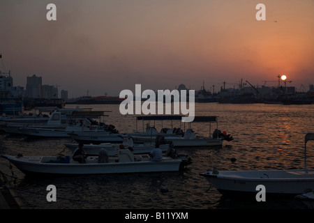 Sharjah Corniche in der Nacht mit der Sonne glitzerte aus dem Wasser mit Booten und Schiffen in den vorderen und hinteren Boden Stockfoto