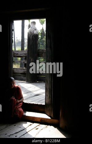 Junger Mönch sitzt in der Tür des Bagaya Kyaung Kloster hergestellt aus Teakholz in Inwa (Ava) in der Nähe von Mandalay, Myanmar (Burma) Stockfoto