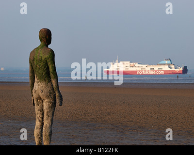 Antony Gormley geschnitzte Figur am Strand mit vorbeifahrenden Schiff auf dem Fluss Mersey, Crosby, Liverpool, Merseyside, England, Vereinigtes Königreich, Stockfoto