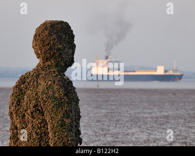 Antony Gormley geschnitzte Figur am Strand mit vorbeifahrenden Schiff auf dem Fluss Mersey, Crosby, Liverpool, Merseyside, England, Vereinigtes Königreich, Stockfoto