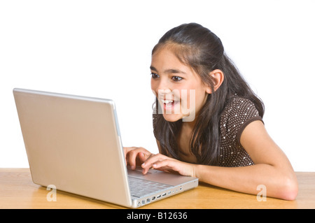 Ein junges Mädchen (10 Jahre) an einem Schreibtisch, einem Lap Top Computer-Bildschirm betrachten und lachen vor dem Hintergrund von reinem weiß (255). Stockfoto