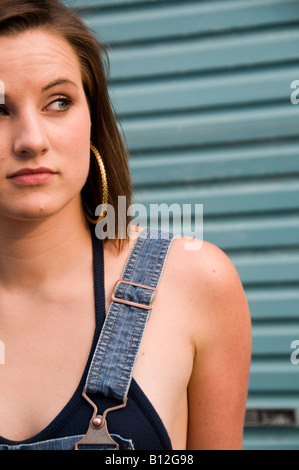 Ziemlich 19 jährige Teenage Mädchen tragen blaue Latzhosen allein durch sich selbst vor blau Metall Garagentor, UK Stockfoto