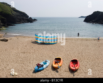 Drei bunte Kanus und ein Windbrecher an einem Sandstrand. Soar Mill Cove, South Hams, South Devon. GROSSBRITANNIEN Stockfoto