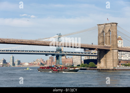 Ein Schlepper Boot treibt eine Frachtschiff unter New Yorker Brooklyn Bridge Stockfoto