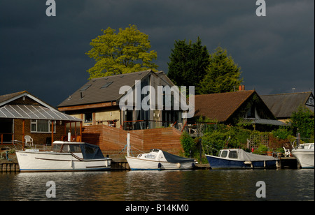 Sportboote vor Anker, bevor am Flussufer Häuser unter schwarzen bedrohlichen Himmel, Themse, Walton on Thames, Surrey Stockfoto