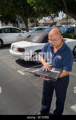 Ein Einsteller wertet Schäden an einem Auto für einen Versicherungsfall Hinweis Laptop und Versicherung Auto im Hintergrund Stockfoto