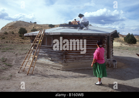 Eine Navajo-Frau schaut zu, wie zwei College-Studenten ein Solarpanel auf ihrem Hogan (Haus) im nördlichen Arizona installieren. Stockfoto