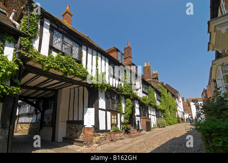 Horizontale Weitwinkelaufnahme der traditionellen Tudor Cottages auf einer gepflasterten Straße in Roggen an einem sonnigen Tag. Stockfoto