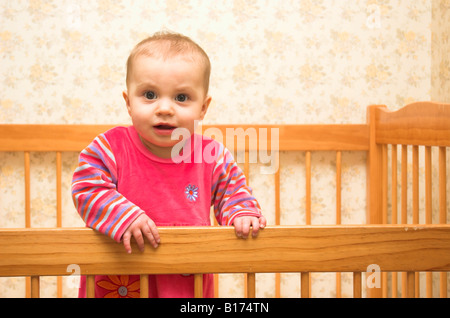 Eine niedliche 9 Monate altes Baby stehend in ihrem Kinderbett Stockfoto