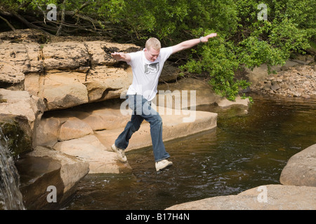 Ein junger Mann springt über Wasser in einem Fluss zwischen zwei Felsen in England, UK, Großbritannien Stockfoto