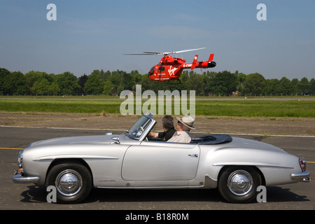 Oldtimerbus Mercedes Benz 190 SL Roadster mit der Jungfrau gesponsert London Air Ambulance Helikopter schwebt im Hintergrund Stockfoto