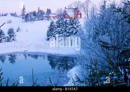 Bauernhaus in der Dämmerung an einem Winterabend Sonne spiegelt sich in Fenstern, auf dem Teich Eis und Schnee bedeckte Bäume, Wiese Bank Prince Edw Stockfoto