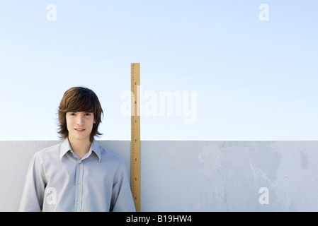 Junger Mann stand neben Maßstab, lächelnd in die Kamera Stockfoto