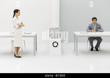 Zwei Profis in Büro, Frau mit verschränkten Armen, Mann, Blick in die Kamera, kreisförmigen Pfeil-Symbol zwischen Ihnen Stockfoto