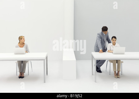 Zwei Frauen, die Arbeiten im Büro, Mann, der hinter einem mit der Hand auf die Schulter Stockfoto