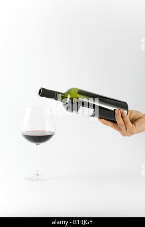 Hand, die Weinflasche über Glas mit einer kleinen Menge Rotwein drin Stockfoto