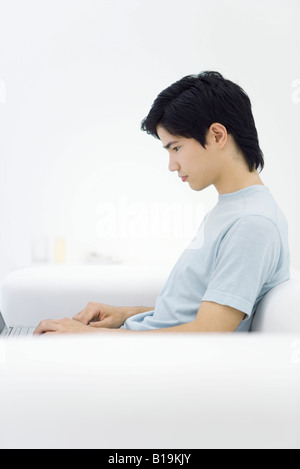 Junge männliche auf Sofa sitzen, mit Laptop, Seitenansicht Stockfoto