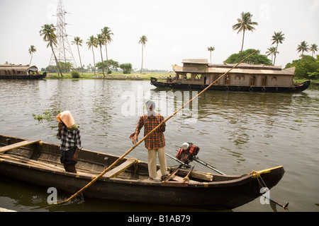 Mann in einem Boot, während ein Hausboot entlang der Grachten in der Nähe von Alappuzha in Kerala, Indien gleitet. Stockfoto