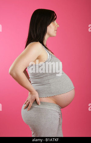 Eine Seite auf einer dunklen Haaren 38 Woche (neun Monate) schwangere Frau stehend Hand auf den Hüften tragen graue Freizeitkleidung. Stockfoto