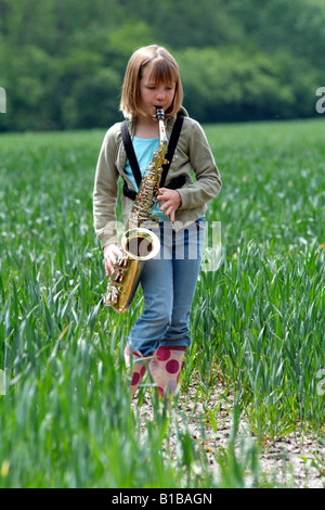 Kleines Mädchen das Saxophon in einem Feld von Kulturpflanzen Walking durch die englische Landschaft Stockfoto