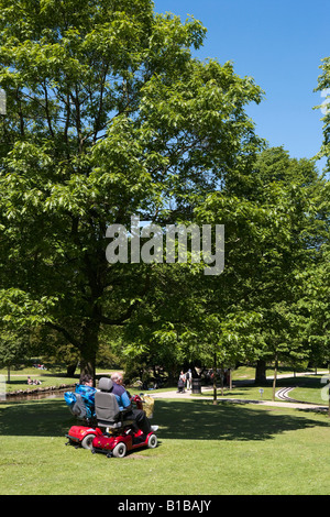 Ältere Paare auf Scooter, The Pavilion Gardens, Buxton, Peak District, Derbyshire, England Stockfoto