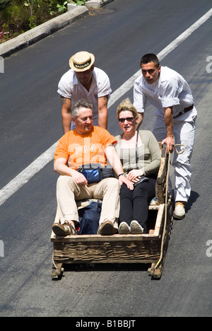 dh Rodelschlittenfahrt MONTE FUNCHAL MADEIRA PORTUGAL Touristenpaar auf Korbkorbschlittenurlauber Stockfoto