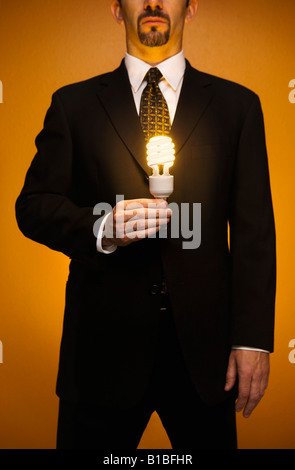 Kaukasische Geschäftsmann im Anzug steht eine beleuchtete kompakte Leuchtstofflampen-Glühbirne in der Hand hält Stockfoto