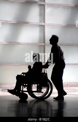 Silhouette einer älteren Frau in einem Rollstuhl und ihre Betreuer Stockfoto